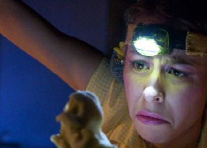 an actor wearing a headlamp staring intently at a small object