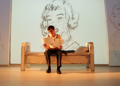 an actor on a bench in front of a projected line drawing of a woman