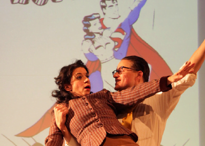 two dancing actors in front of cartoon projection of superman