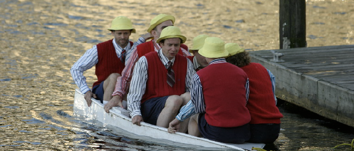 six actors with yellow hats and red vests in a wee sinking boat
