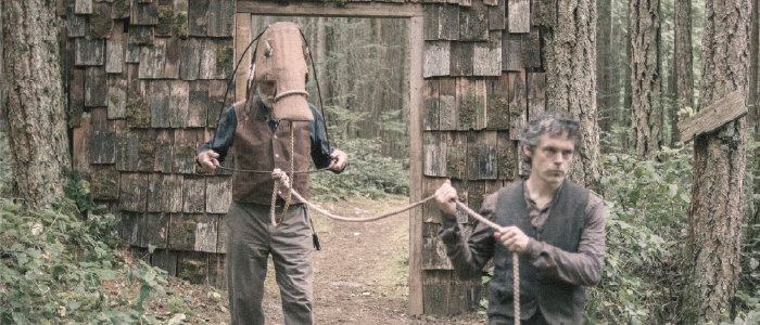 an actor leading a horse puppet thru a door way in the forest