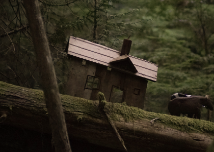 Closeup of a model house and puppet oxen on a mossy log in the woods. Photo by Sophia Dagher.