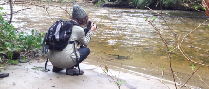 a women crouching while taking photos of a river