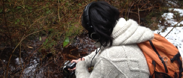 a woman in a white sweater and orange backpack crouching down in the forest and listening