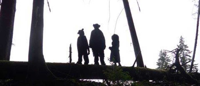 silhouette of three small scale puppet people on a log in a forest