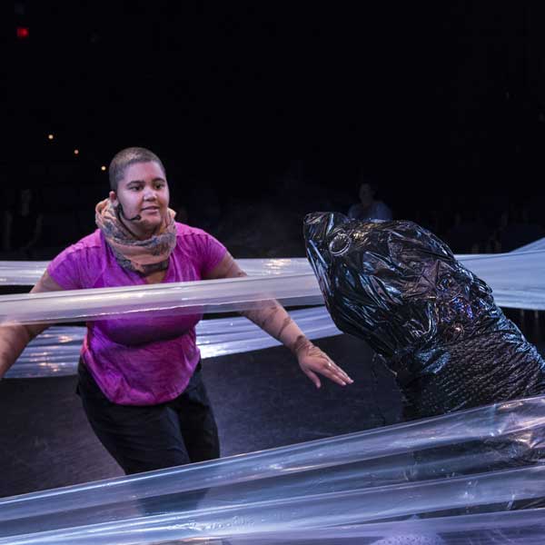 actress in the middle of waves made of plastic strands, interacting with a seal also made of plastic bags