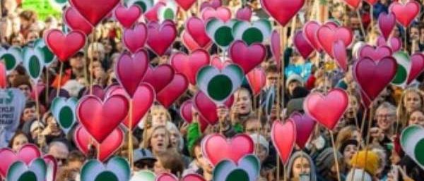 A large crowd of people holding up signs shaped like hearts.