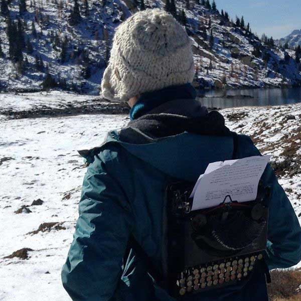 person with a typewriter on their back, facing the snowy mountain in the background