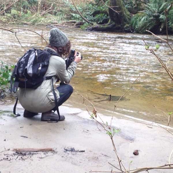 a person crouching down while taking a picture of a river